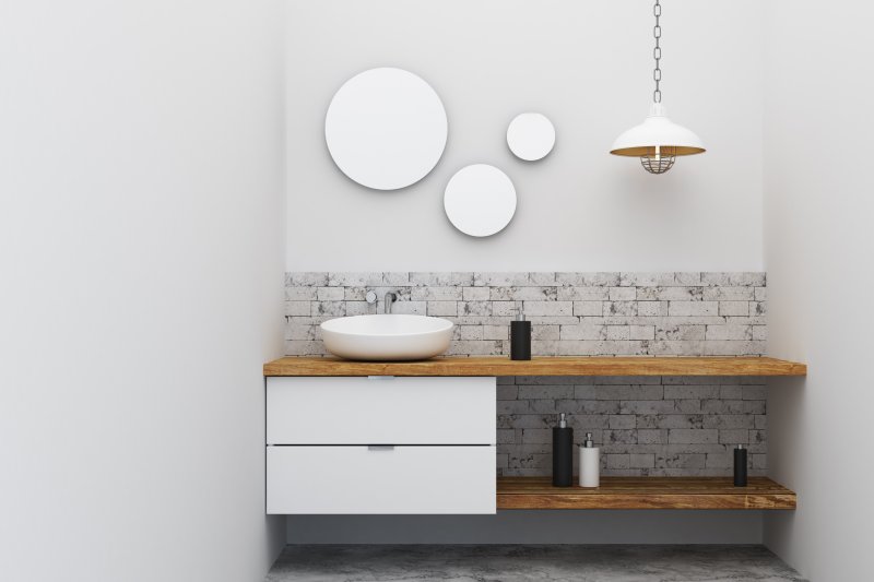 Industrial vessel bathroom sink on wood vanity below industrial pendant lamp and three mirrors (Photo by peshkova – stock.adobe.com)