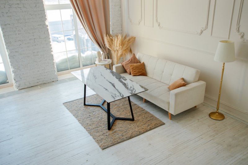 overhead view of living room with light wood laminate flooring, tan rug, white couch, and sunny windows (Photo by Ekaterina Morozova / EyeEm via Getty Images)