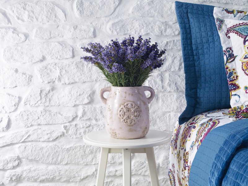 closeup of bunch of lavender in vase on white stool next to colorful bed against white brick wall (Photo by gerenme/iStock / Getty Images Plus via Getty Images)
