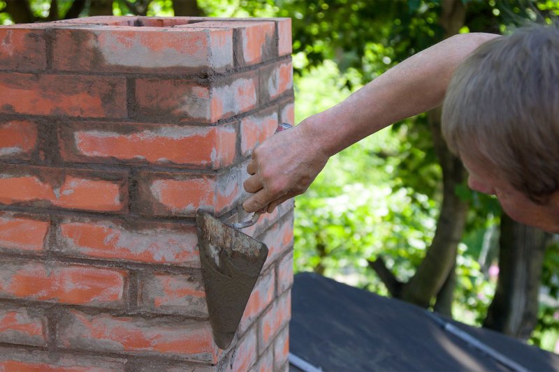 man patching up cracks on chimney roof (Photo by zabavna - stock.adobe.com)