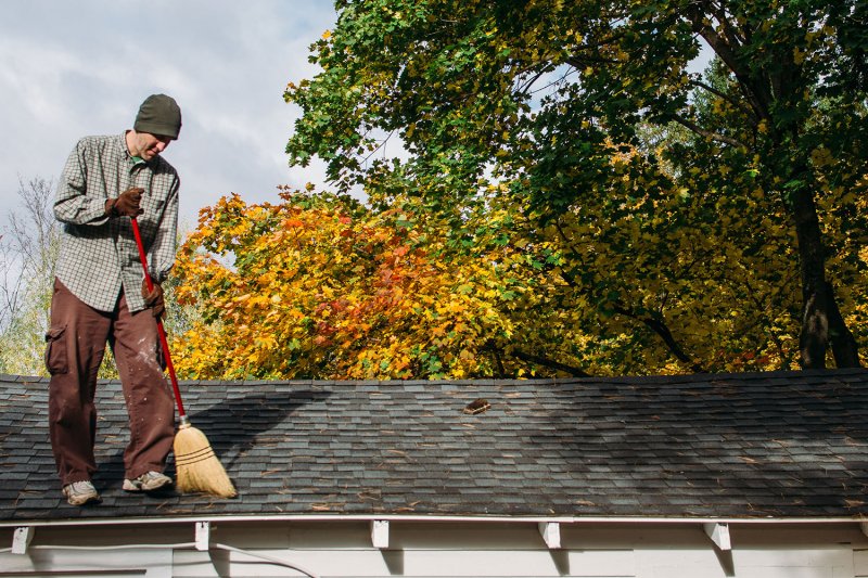 man sweeping leaves on roof (Photo by Deirdre Malfatto/Stocksy - stock.adobe.com)