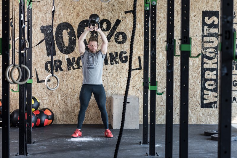 Man in gym clothes working out with a kettlebell in a garage home gym with an inspirational quote painted on the wall behind him (Photo by Photographee.eu - stock.adobe.com)