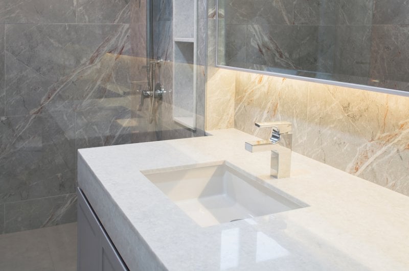 a white quartz bathroom countertop with rectangular shapes, silver fixtures, and tan and gray marbled walls (Photo by nongnuch_l - stock.adobe.com.)