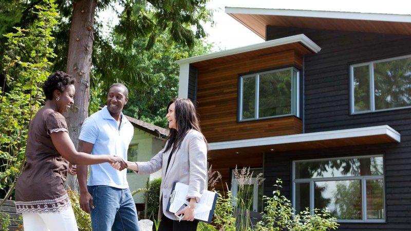 Real estate agent greeting couple at house (Photo by Noel Hendrickson via Getty Images)