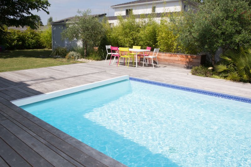 partial view of rectangular pool with concrete patio area and colorful patio furniture in background (Photo by OceanProd - stock.adobe.com)