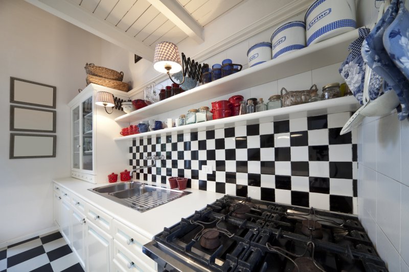Kitchen with black-and-white checked tile backsplash, white cabinets, and retro tins on white open shelves (Photo by Javani LLC - stock.adobe.com)