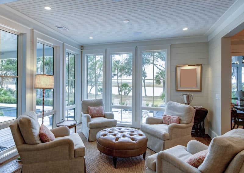 Sitting room with four armchairs facing each other, leather ottoman, shiplap accent wall and floor to ceiling windows (Photo by Wollwerth Imagery - stock.adobe.com)