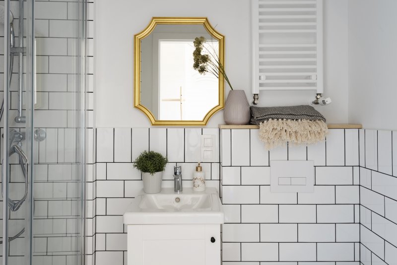 Small bathroom with white subway tiles, bathroom sink and stylish gold mirror on the wall (Photo by photosbysabkapl – stock.adobe.com)