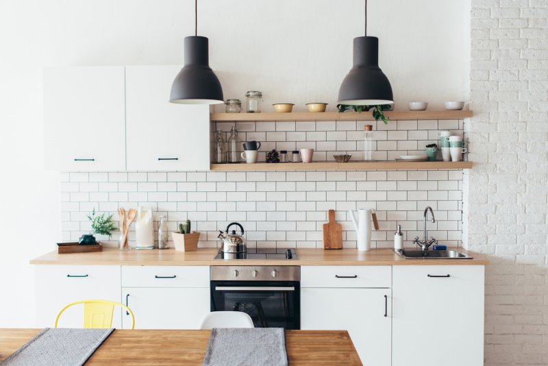 Modern kitchen with white subway tile backsplash, white cabinets, wood open shelves and black pendant lights (Photo by undrey - stock.adobe.com)