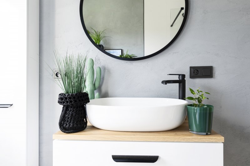 Small vessel sink with black faucet and green plants underneath a round black mirror (Photo by photosbysabkapl – stock.adobe.com)