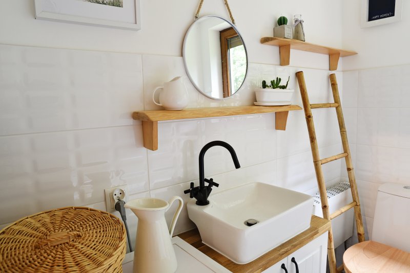 Bathroom with wooden ladder next to toilet, open wood shelves, small square sink, and white tile (Photo by photosbysabkapl – stock.adobe.com)