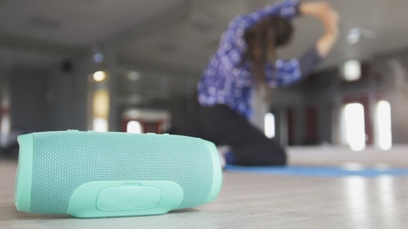 A woman stretching on the floor of her home gym with a turquoise wireless speaker (Photo by Barselona Dreams - stock.adobe.com)