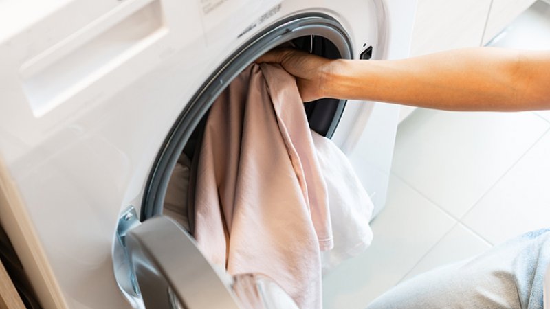 A woman’s hand puts clothes into a washing machine (Photo by Pattarisara - stock.adobe.com)