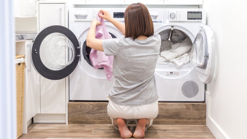 A woman adds clothes from washing machine to the dryer (Photo by Mariakray - stock.adobe.com)