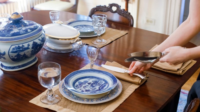 A woman’s hand setting the table with antique tableware (Photo by Julien Mcroberts via Getty Images)
