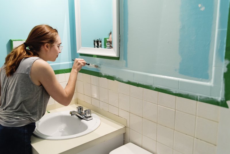 Woman painting bathroom with paintbrush (Photo by martinedoucet /E+ via Getty Images)