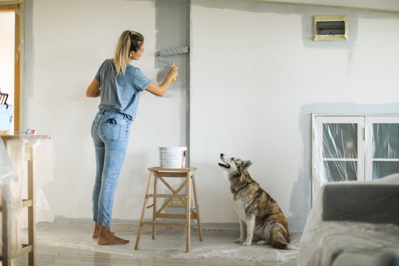 Woman painting indoors next to dog (Photo by svetikid /E+ via Getty Images)