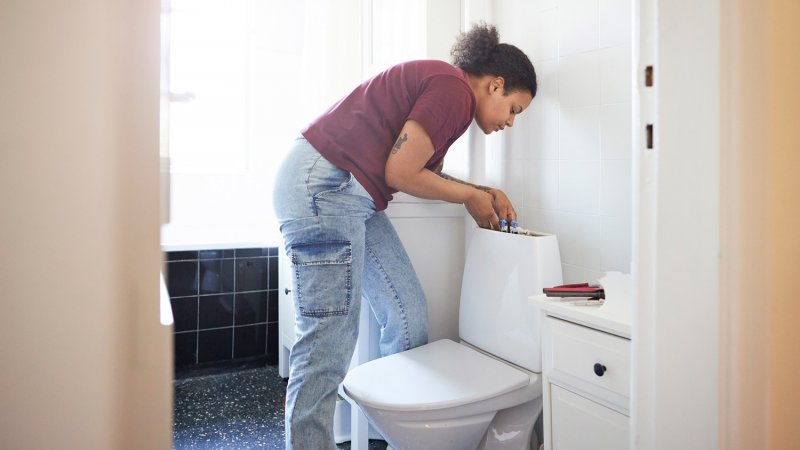 Woman repairing toilet in home bathroom (Photo by Klaus Vedfelt / DigitalVision via Getty Images)