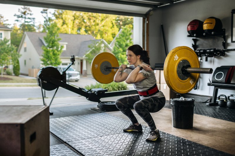 Young woman in gym clothes weight lifting in her garage home gym surrounded by gym equipment (Photo by IngredientsPhoto / E+ via Getty Images)