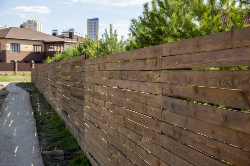 a wooden privacy fence running along grass and sidewalk on a suburban street (Photo by Татьяна Антоненко - stock.adobe.com)