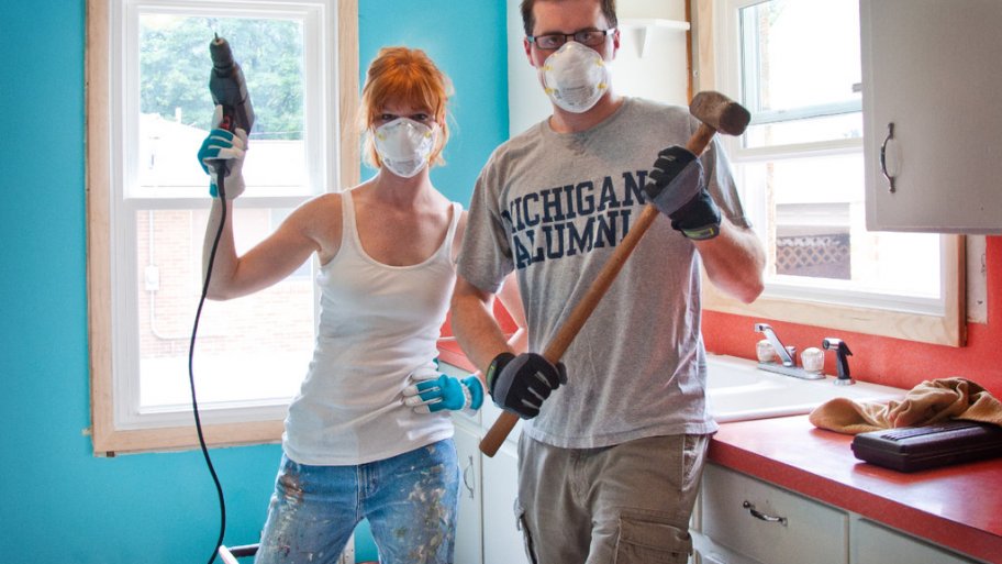 woman and man wearing air filter masks and holding a drill and sledgehammer