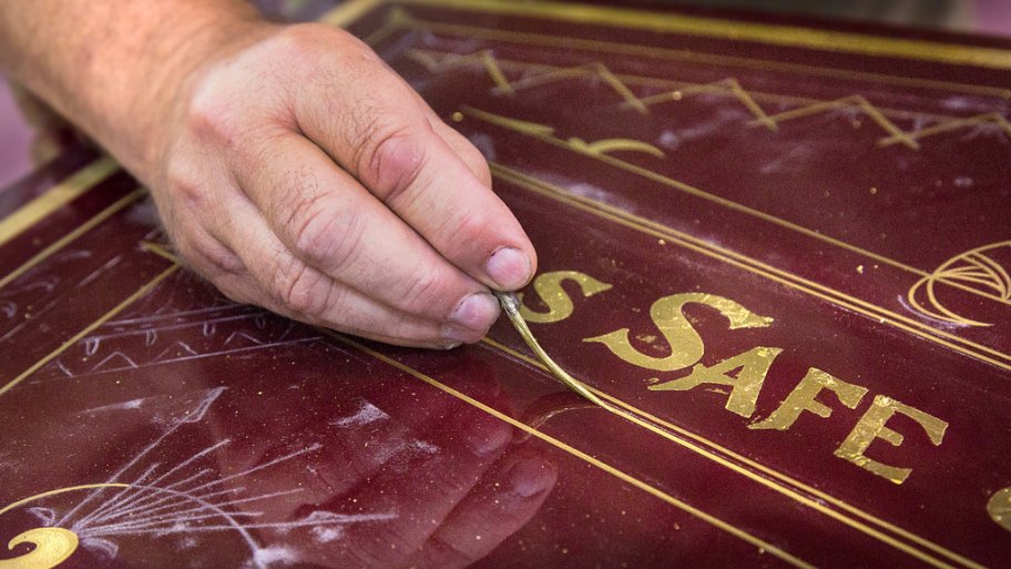 Man's hand applying gold pinstriping on an antique safe from Hall's in Cincinnati, Ohio