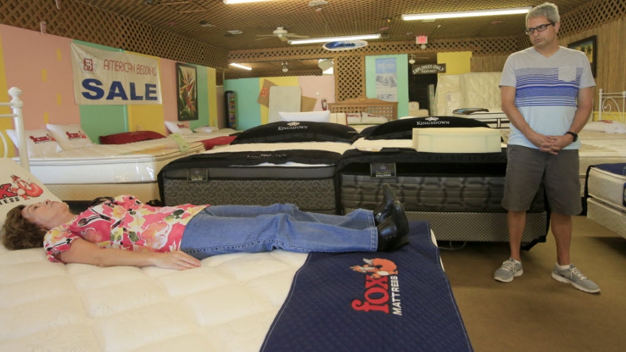 a woman laying on a bed as her friend watches as a mattress shop