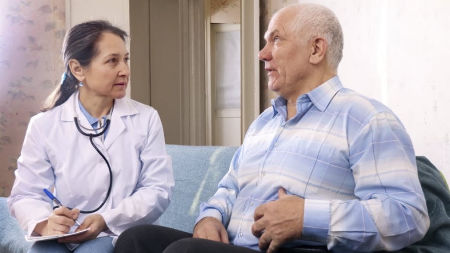 a female doctor takes notes as a elderly male patient explains stomach symptoms.