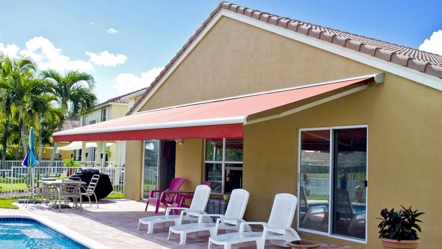retractable awning covers poolside patio area with lounging chairs in the backyard of a house.