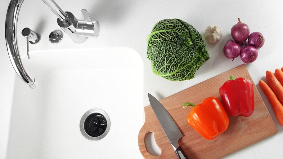 garbage disposal in sink with vegetables and knife on cutting board