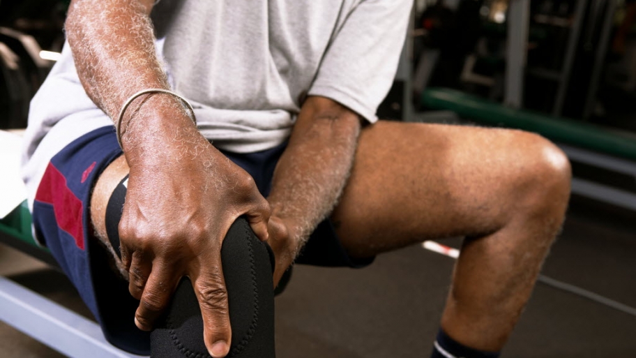 man sits on bench at fitness center massaging his knee.