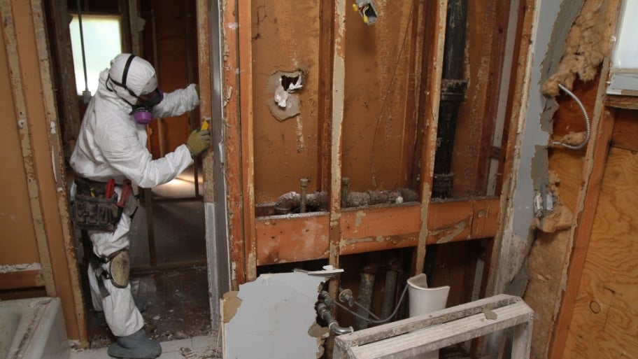 A man in a mold remediation uniform removes drywall from a bathroom to clear mold out of a home.