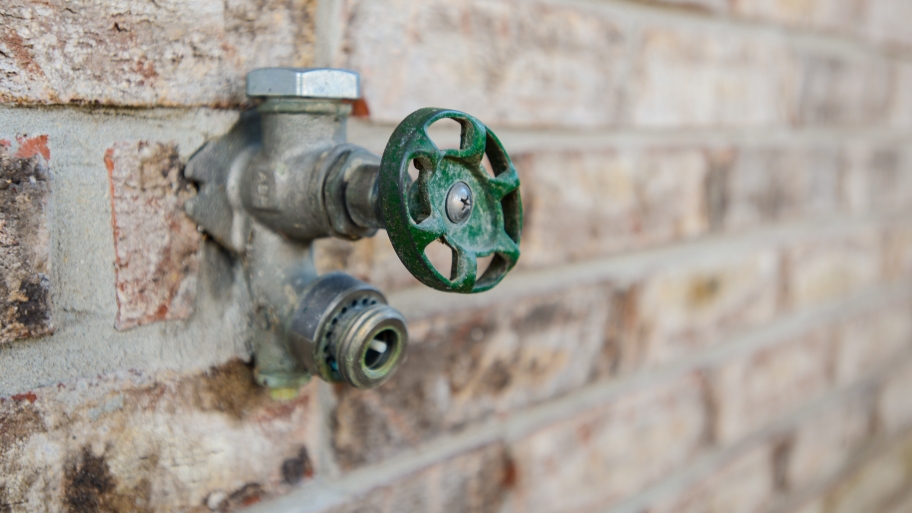 blue handled outdoor faucet on a brick wall