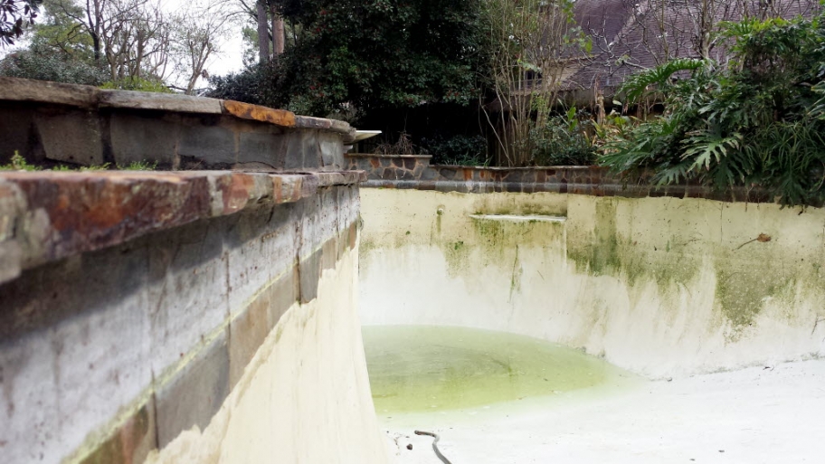 a drained pool with cloudy water and algae buildup stains on the pool wall.