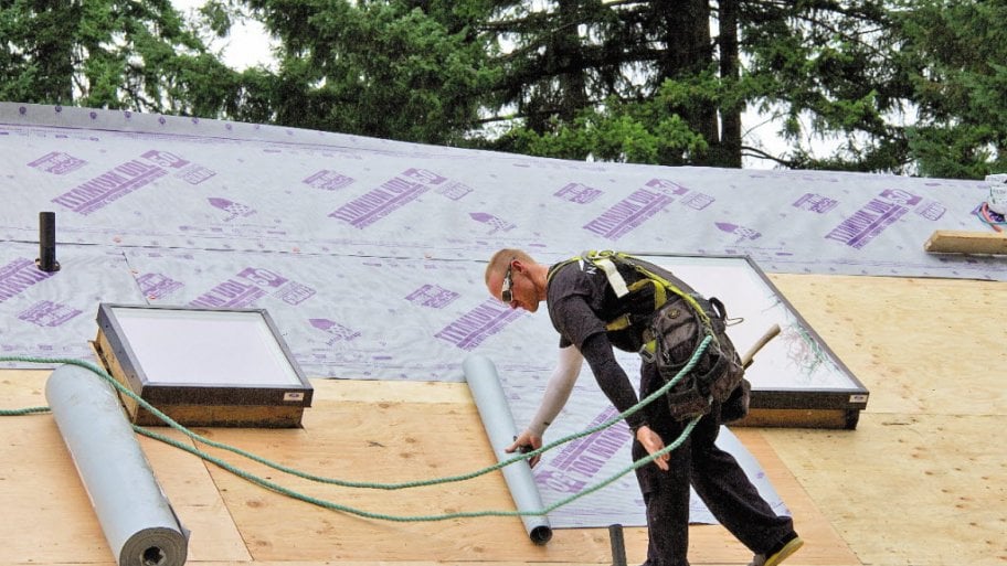 A man lays underlayment on a roof deck.
