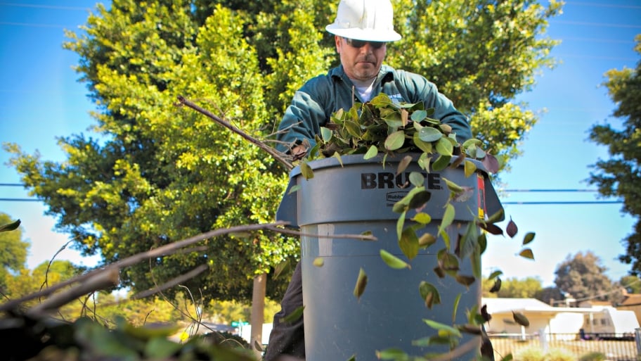 man putting leavs in a trash bin