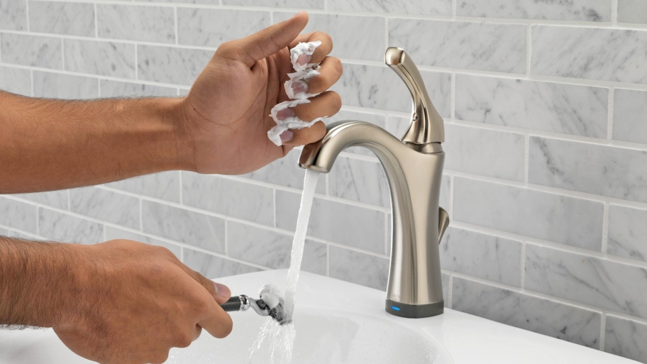 Man rinsing of razor under bathroom faucet.