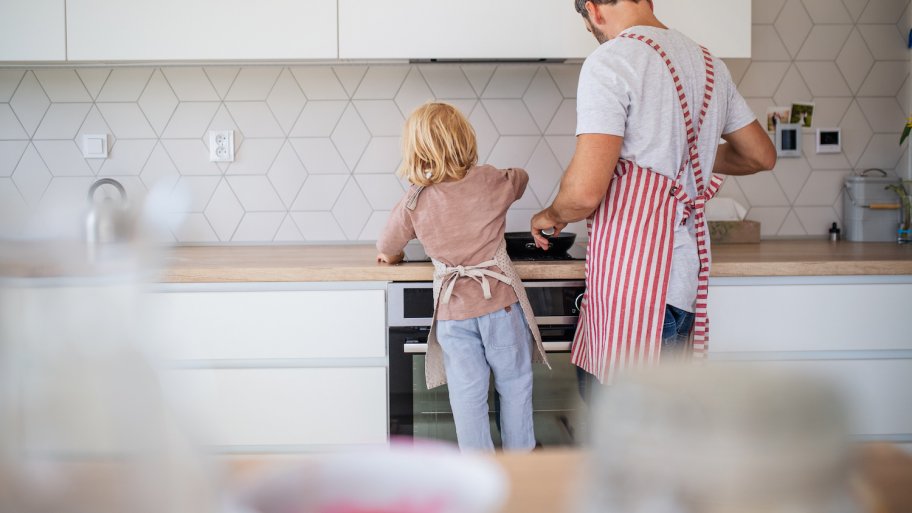 All-white kitchen with white geometric tile backsplash and a father and child cooking together at the stove