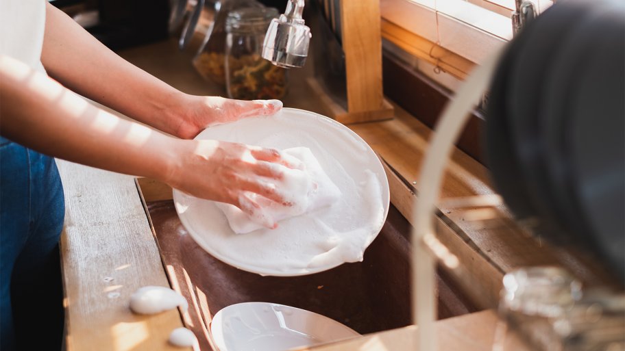 Person using dish soap and sponge to wash a plate