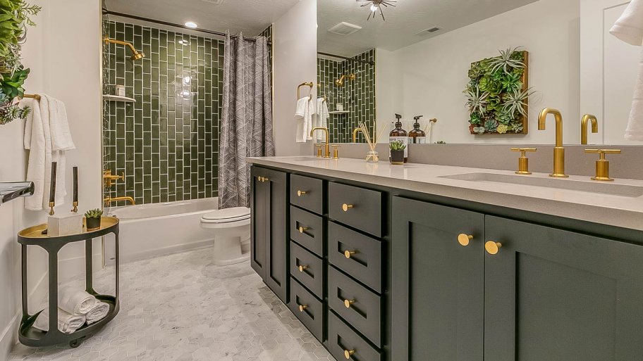 A bathroom with green tiles and brass faucets