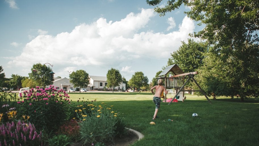 young boy in grassy backyard with play set in background