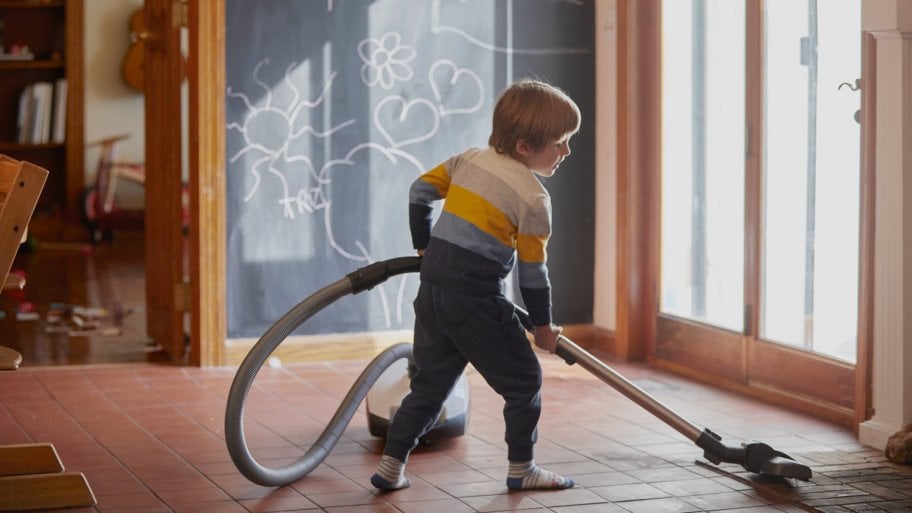 A boy with a vacuum in a room with ceramic tiles for flooring