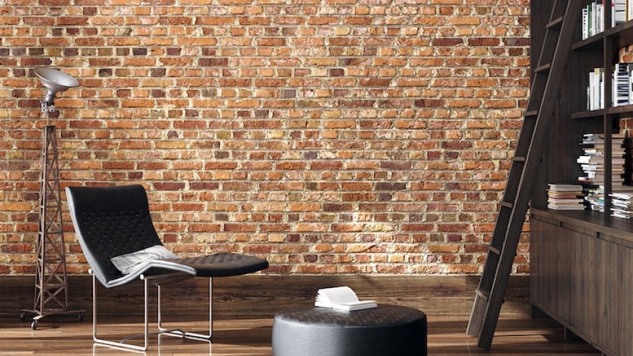 a brick wall and wood floor room with black modern reading chair and lamp, ottoman, and bookshelf with ladder