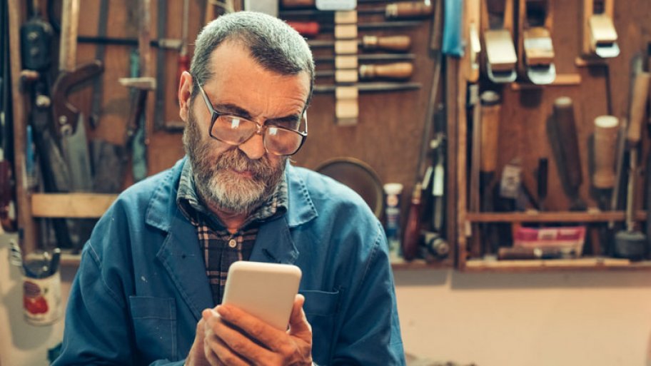 Senior man with beard in the workshop text messaging on mobile
