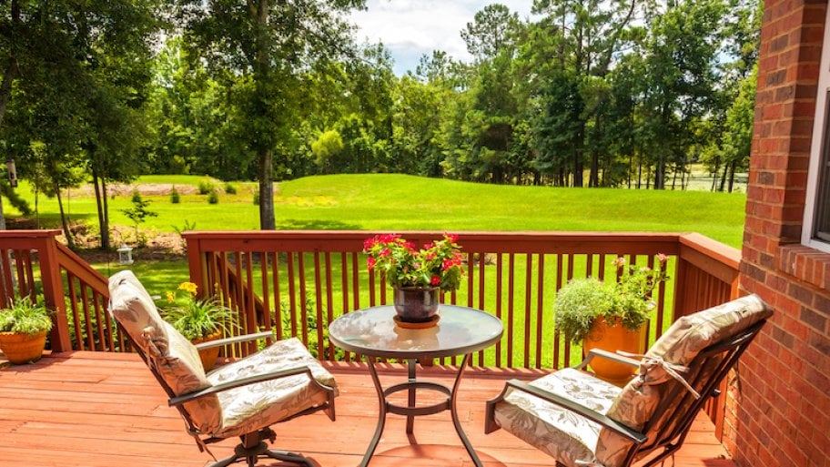 a cedar deck with two patio chairs and a small table overlooking a lush green yard