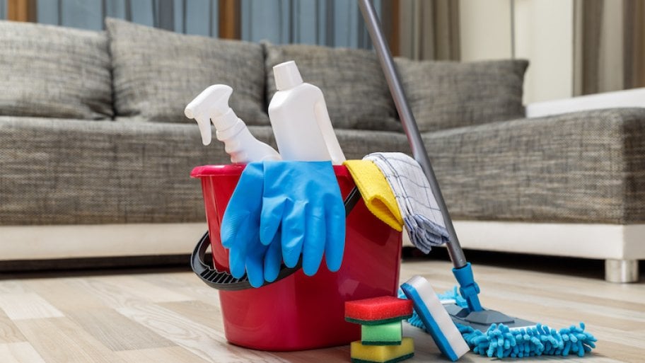 bucket of cleaning supplies sits on light wood floor in front of grey couch