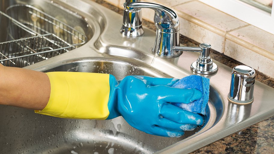 yellow-gloved hand cleaning kitchen sink