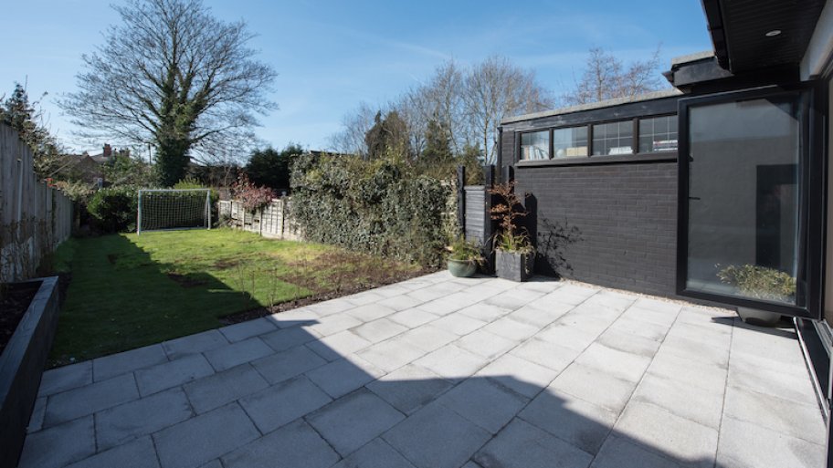 concrete patio opens up to grassy yard area surrounded by vine covered fences