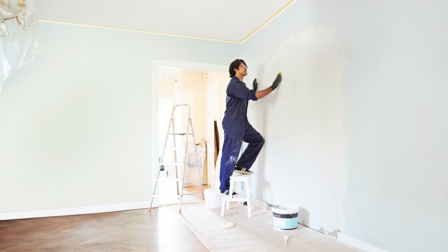 A contractor standing on a ladder while applying plaster on wall