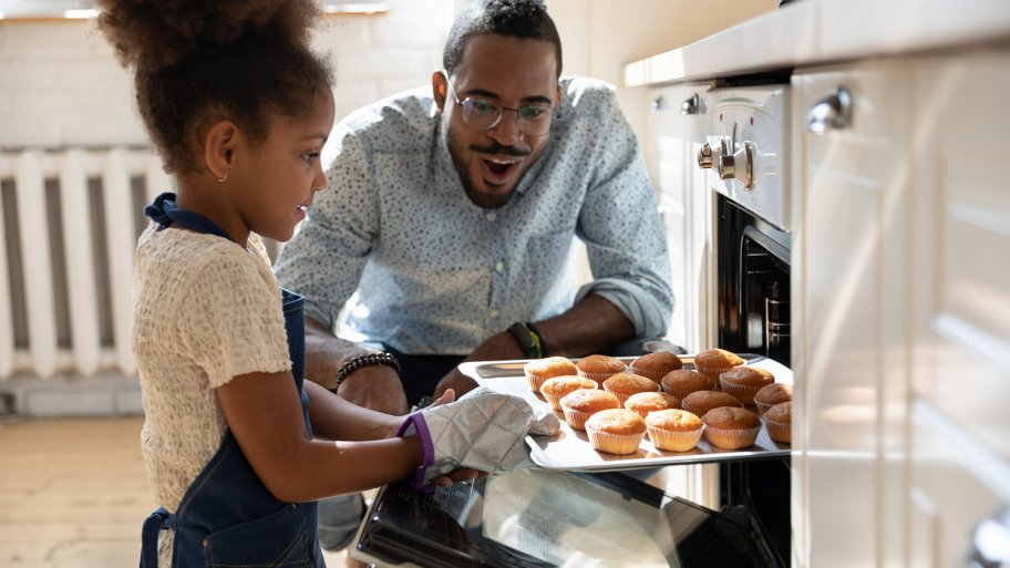 Dad watches daughter pulled baked muffins from oven (Photo by fizkes / iStock / Getty Images Plus via Getty Images)